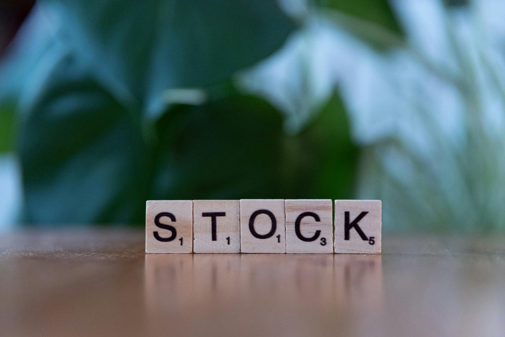 Close-up of wooden letter blocks spelling 'STOCK' on a table against a blurred green background.